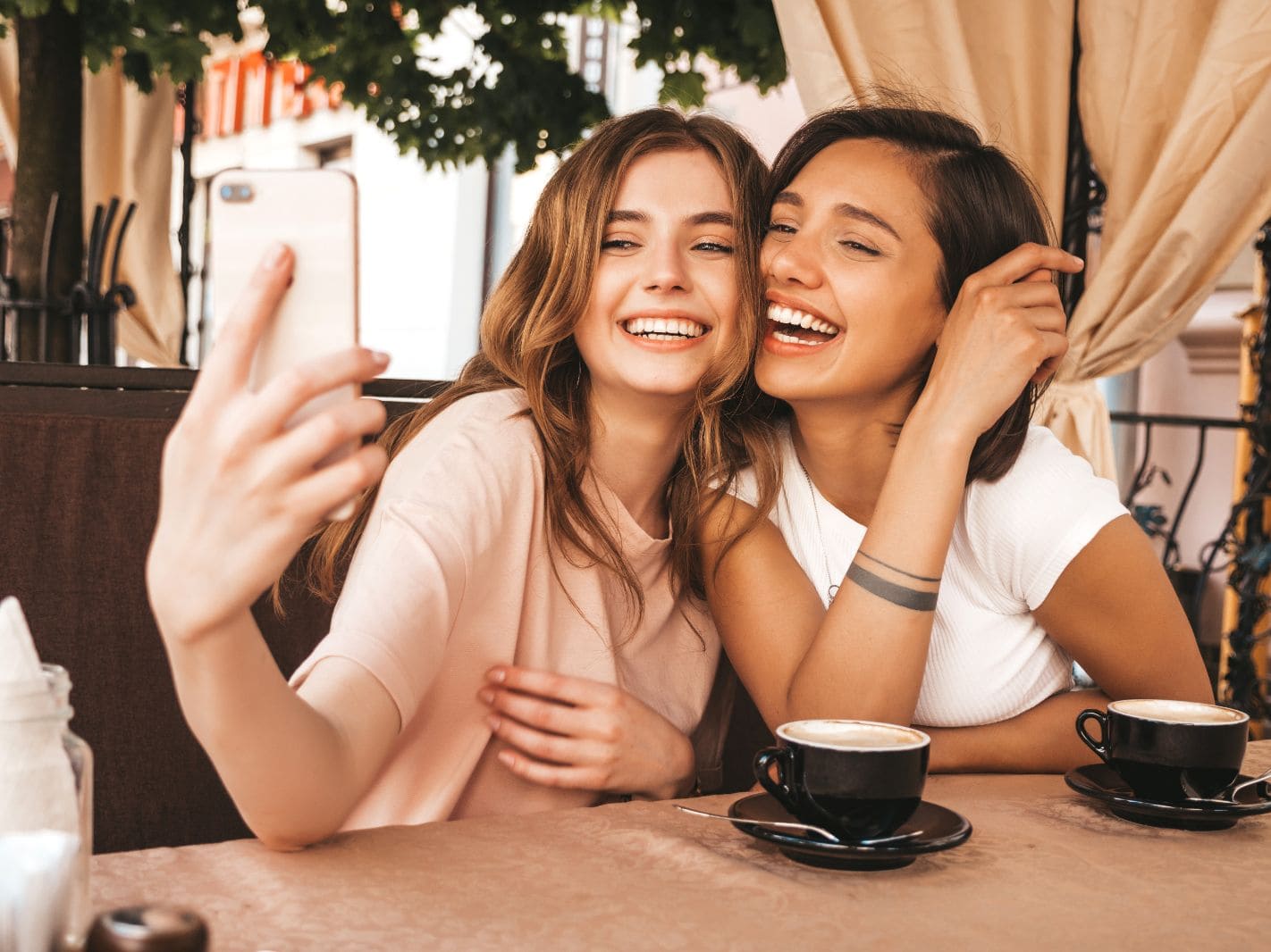 two-young-beautiful-smiling-hipster-girls-trendy-summer-clothes-carefree-women-chatting-veranda-cafe-drinking-coffee-positive-models-having-fun-taking-selfie-smartphone (1)