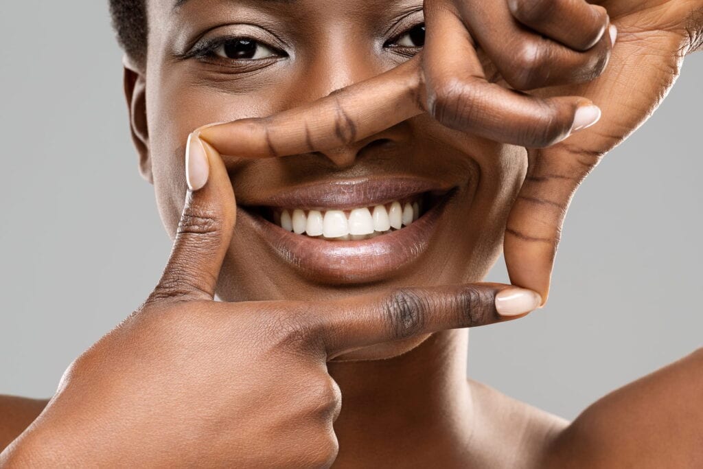 A woman shows off her bright, picturesque smile while holding up her hands in the shape of a picture frame.