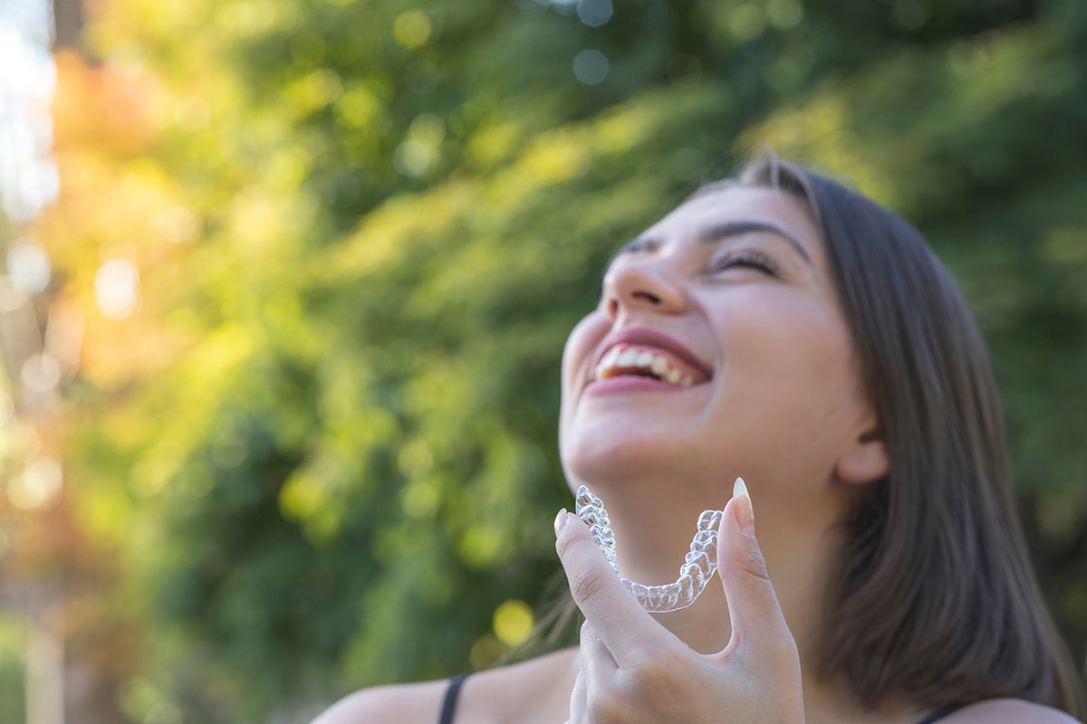 A-smiling-woman-holding-her-Invisalign-aligner
