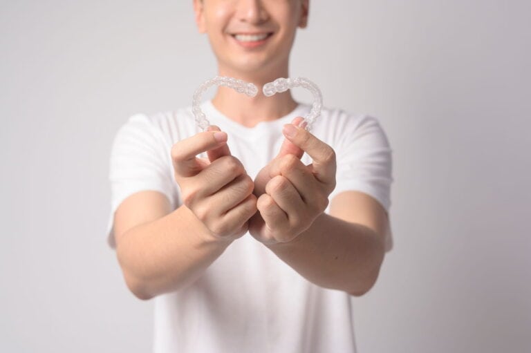 A young man holds his Invisalign retains in a heart shape.