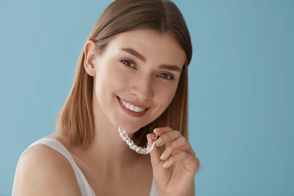 A young woman holds up her retainer.
