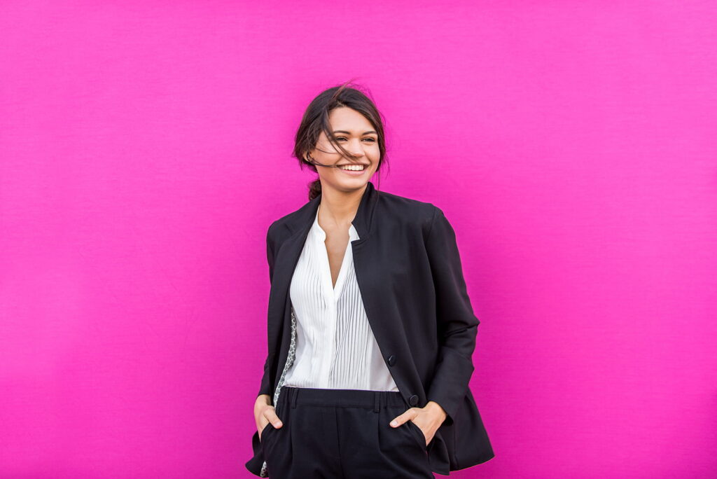 Woman smiling with pink background after getting Can You Get Invisalign with a Crown