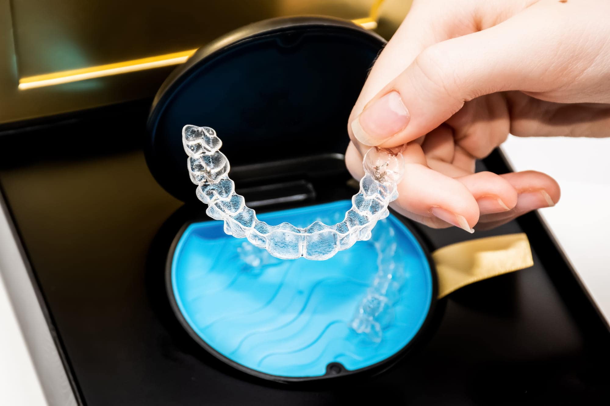 A person holds up an Invisalign retainer in its case.