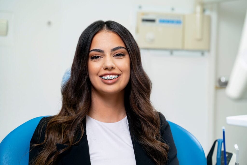 An elegant woman sits in an orthodontist's chair, showing off her braces and gorgeous smile.