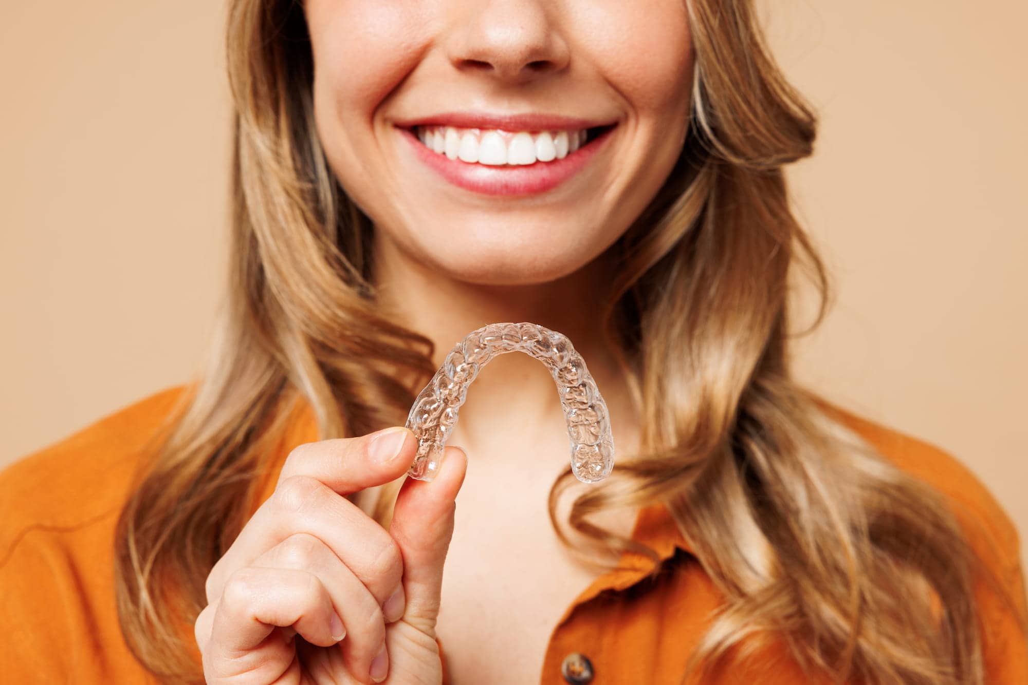 A woman smiling holding an invisalign 